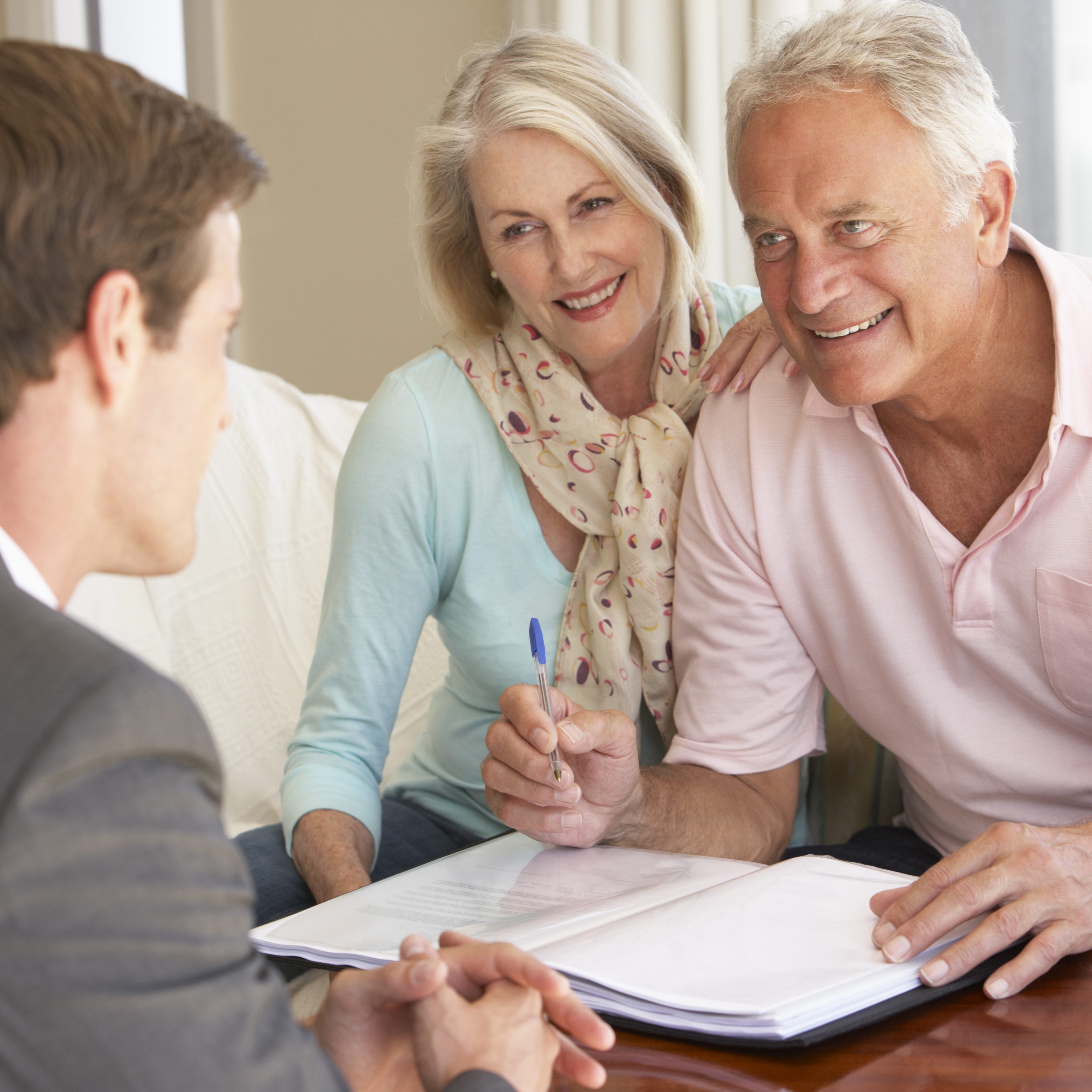 Senior Couple Meeting With Financial Advisor At Home And Smiling
